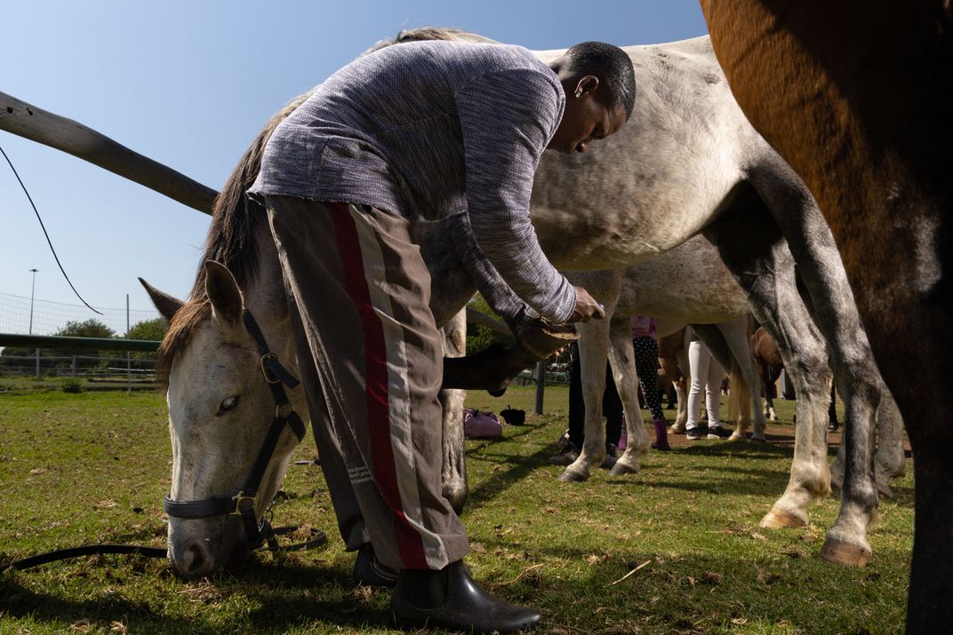 Trainee Kabelo uses a hoofpick to remove debris from a horse’s hooves.