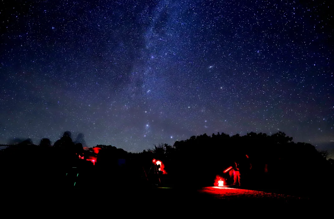 People setting up telescopes against a backdrop of a starry night sky