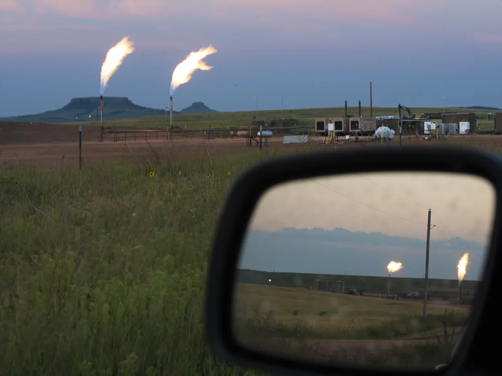 View of flaring at an oil well through a car window and through its side view mirror