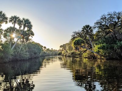 Trees line a winding river, and the blue sky is reflected in the water