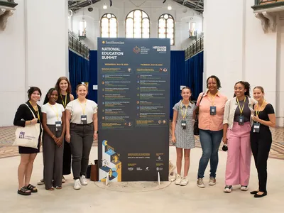 A group of teachers gather around a large blue billboard of the Summit schedule